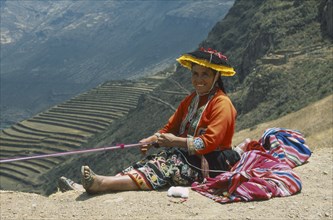PERU, Cusco, Pisac, "Quechuan Indian woman weaving, inca terracing behind. Sacred Valley"