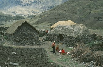 PERU, Cusco, Cancha Cancha, Local Quechuan people weaving in front of dwelling.