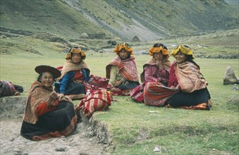 PERU, Cusco, Cancha Cancha, "Local Quechuan women sat on grass, wearing traditional dress."