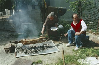 GREECE, Attica, Nea Makri, A couple roasting a lamb traditionally over coals outside at Easter.