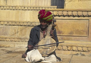 INDIA, Rajasthan, "Jaisalmer,", "Musician with Sitar, sat on the ground outside a building."