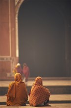INDIA, Uttar Pradesh, Agra, Two woman sat talking in front of one of the red sand stone buildings