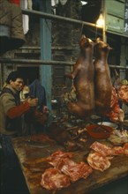 CHINA, Guangzhou, Dogmeat hanging in meat market with seller behind stall