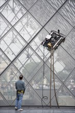 FRANCE, Ile de France, Paris, Workman watching robot window cleaning machine on the pyramid at the