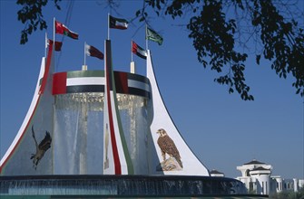 UAE, Abu Dhabi, Falcon Fountain with flags flying on the top framed by  tree branches. Part of the