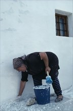 SPAIN, Andalucia, Andalucian village woman white washing the exterior wall of her home.
