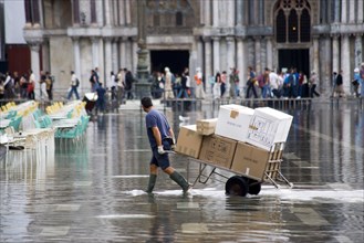 ITALY, Veneto, Venice, Aqua Alta High Water flooding in St Marks Square with a delivery man pulling