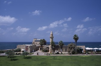ISRAEL, Caesarea, The Herodian Harbour with eastern view of stone buildings with palm trees and