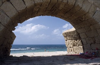 ISRAEL, Caesarea, Roman Aqueduct with view through a single arch towards sunbathers on the beach