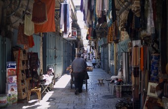 ISRAEL, Jerusalem, An Arab man pushing his bread cart through a narrow street between clothes and