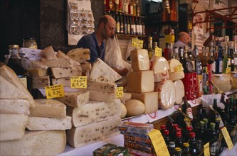 ITALY, Sicily, Catania, Market cheese stall with a male stall holder displaying a selection of