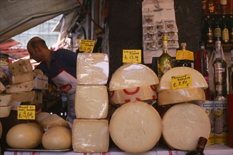 ITALY, Sicily, Catania, Market cheese stall with male stall holder displaying a selection of