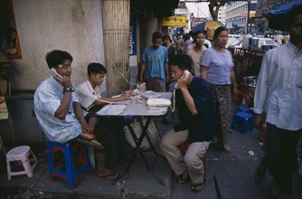MYANMAR, Yangon, Public telephone exchange.  Young men using telephones set up on folding table on