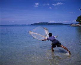 THAILAND, Krabi, Ao Nang Beach.  Fisherman standing in shallows casting net into sea