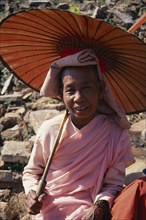 MYANMAR, Mingun, Portrait of nun wearing traditional pink robes holding locally made parasol.
