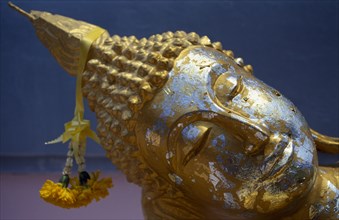 THAILAND, Koh Samui, Bophut, Head of reclining Buddha with gold leaf and floral offering.