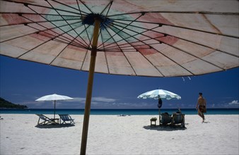 THAILAND, Phuket, Western tourists on white sand beach with sun loungers part framed by umbrella in