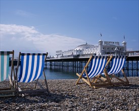 ENGLAND, East Sussex, Brighton, Blue and white striped deckchairs on pebble beach over looking