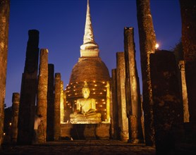 THAILAND, Sukhothai, Colonnade leading to massive seated Buddha and stupa illuminated at dusk