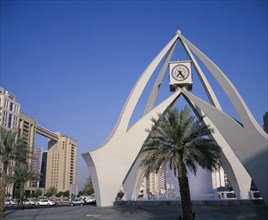 UAE, Dubai, Dubai Clock Tower.  Modern sculptural structure with pool and fountains below and palm