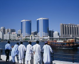 UAE, Dubai, Dubai Creek.  Men standing on waterfront looking out towards city skyline and passing