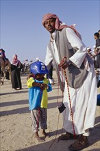 KUWAIT, Sport, Man with young child jockey dressed in racing silks at camel racing event.