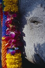 THAILAND, Bangkok, Flower garland offering hanging over stone elephant statue.