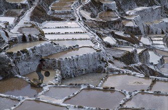 PERU, Cusco, Salinas, Man working on salt terraces near Maras used to collect salt by evaporation