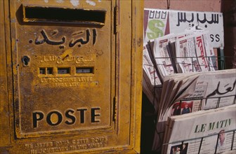 MOROCCO, Marrakech, Close cropped view of postbox beside rack of French and Arabic newspapers.