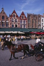 BELGIUM, West Flanders, Bruges, The Markt (Market Place).  Horse drawn carriage passing line of