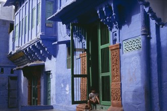 INDIA, Rajasthan, Jodhpur, Detail of blue painted house with child sitting in open doorway with