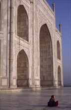 INDIA, Uttar Pradesh, Agra, Taj Mahal.  Part view of white marble exterior with woman sitting on