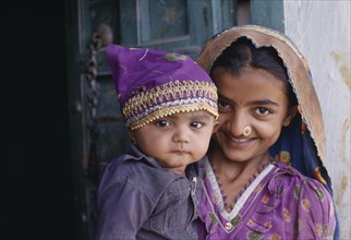 INDIA, Gujarat, Kutch, Dhordo Village.  Girl with nose ring holding young child.