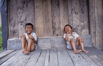 INDONESIA, Sumatra, Children, Two laughing children sitting on wooden floor of building.