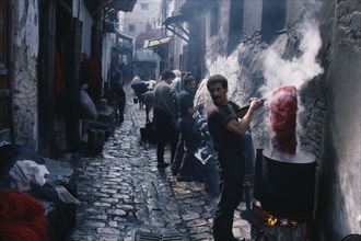 MOROCCO, Fez, Street in the wool dyeing souk with man in foreground lifting skein of yarn from vat