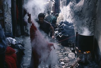 MOROCCO, Fez, Street in the wool dyeing souk with man in foreground lifting skein of steaming yarn