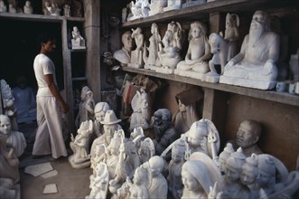 INDIA, Rajasthan, Jaipur, Marble carver in workshop with shelves of statues.