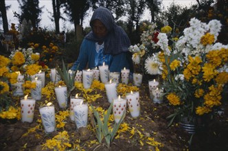 MEXICO, Michoacan, Purepecha, Tarascan Indian woman lighting candles on grave decorated with