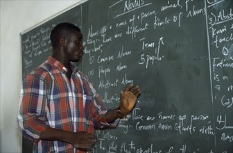 NIGERIA, Kano, English teacher standing beside blackboard giving grammar lesson.