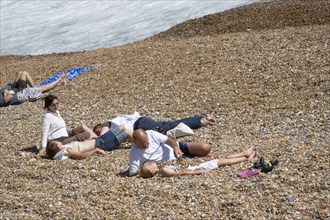 ENGLAND, East Sussex, Brighton, Family on the stoney beach at Hove with father covering son with