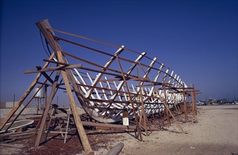 QATAR, Industry, Traditional dhow boat building.  Man standing below wooden frame.