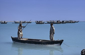 QATAR, Khor, Fishermen in a wooden canoe with fishing boats at anchor beyond