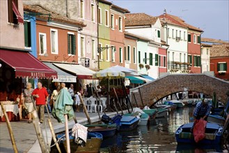 ITALY, Veneto, Venice, Colourful houses beside a canal on the lagoon island of Burano with people