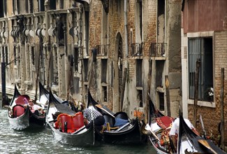 ITALY, Veneto, Venice, Gondoliers resting with their gondolas moored at the edge of the Rio Dei