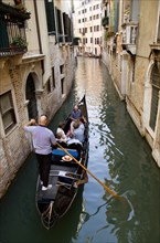 ITALY, Veneto, Venice, Gondolier carries sightseeing tourists in his gondola along a norrow canal