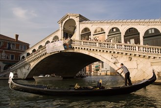 ITALY, Veneto, Venice, An empty gondola passes in front of the Rialto Bridge over the Grand Canal