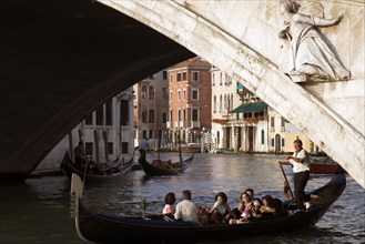 ITALY, Veneto, Venice, A gondola carrying tourists passes beneath the Rialto Bridge over the Grand