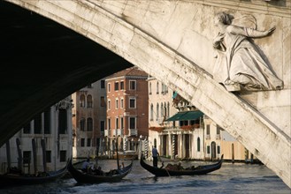ITALY, Veneto, Venice, A gondola carrying tourists passes beneath the Rialto Bridge over the Grand