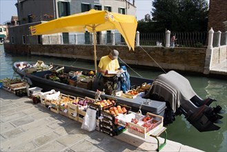 ITALY, Veneto, Venice, A fruit and vegetable vendor with his boat moored alongside the Fondamenta