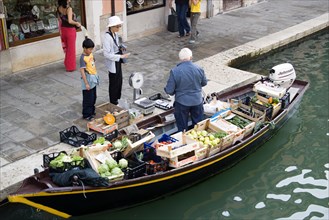 ITALY, Veneto, Venice, A fruit and vegetable vendor serving a customer from his boat moored